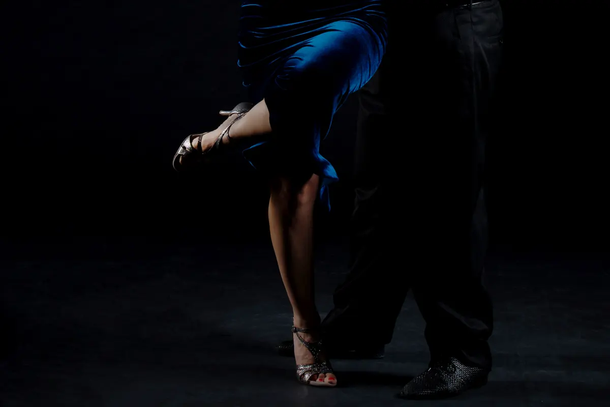 Dettaglio delle gambe di una coppia di tango argentino, lei in abito blu su fondo scuro