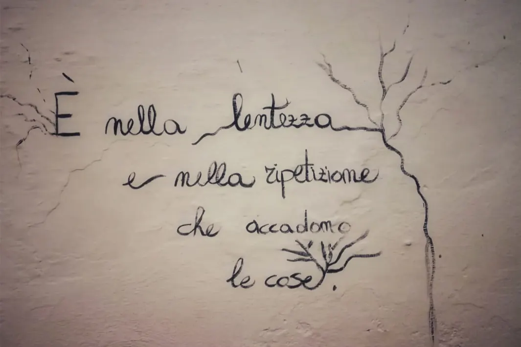 Una scritta a mano su un muro: «È nella lentezza e nella ripetizione che accadono le cose»