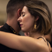 Coppia in abbraccio di tango argentino, il viso di lei di profilo appoggiato alla guancia di lui