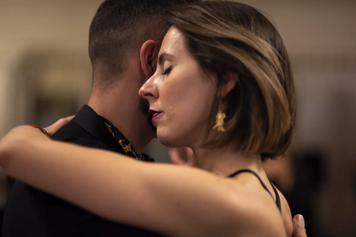 Coppia in abbraccio di tango argentino, il viso di lei di profilo appoggiato alla guancia di lui